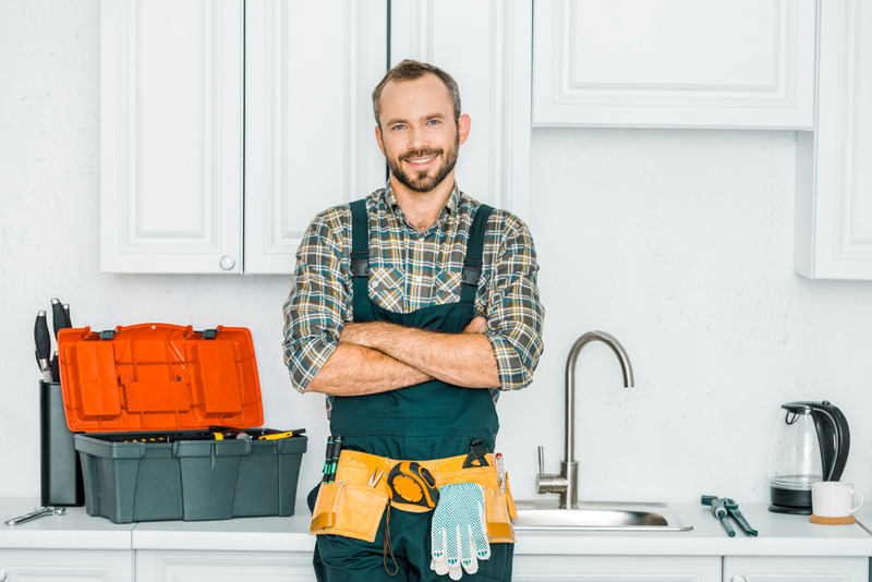 Zufriedener Installateur mit Werkzeuggürtel steht in moderner Küche neben Werkzeugkiste.