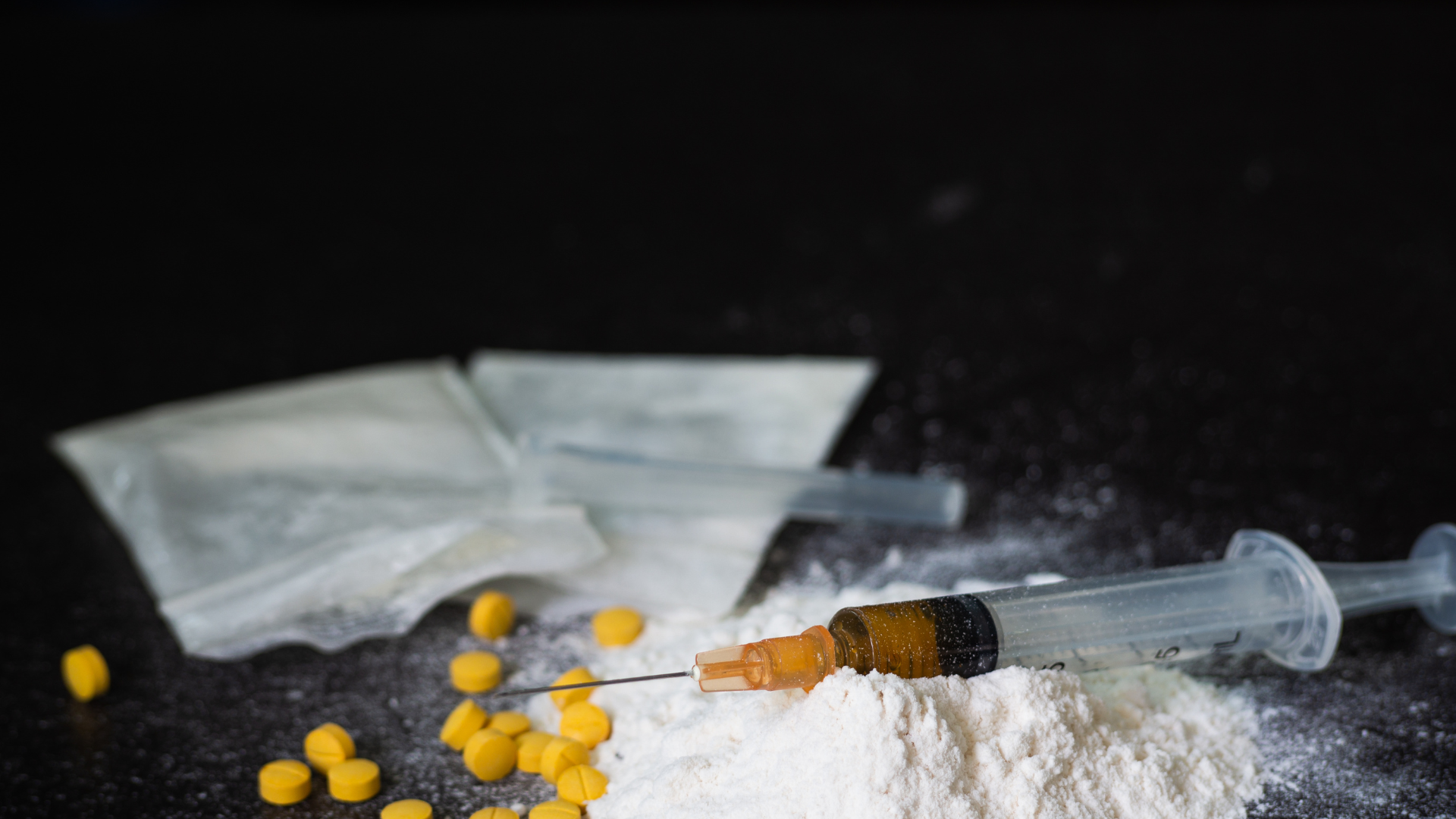 needle on top of white powder with yellow pills and small bags
