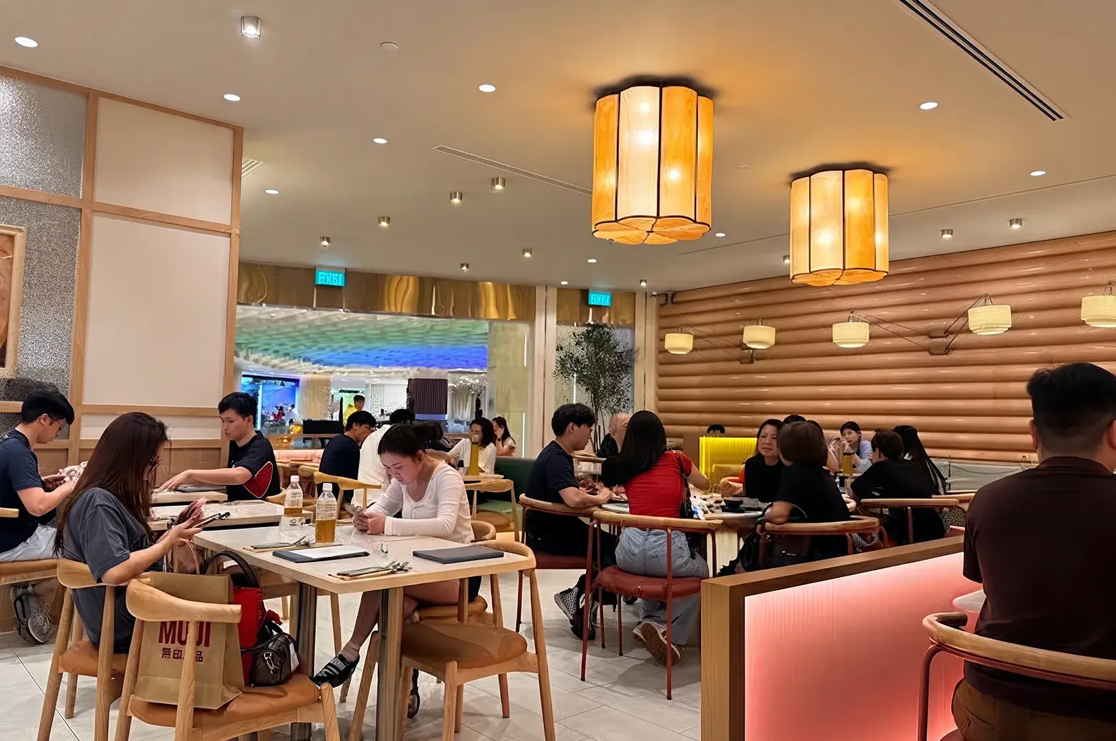 Warmly lit restaurant dining room packed with patrons seated at wooden tables under large lantern lights.