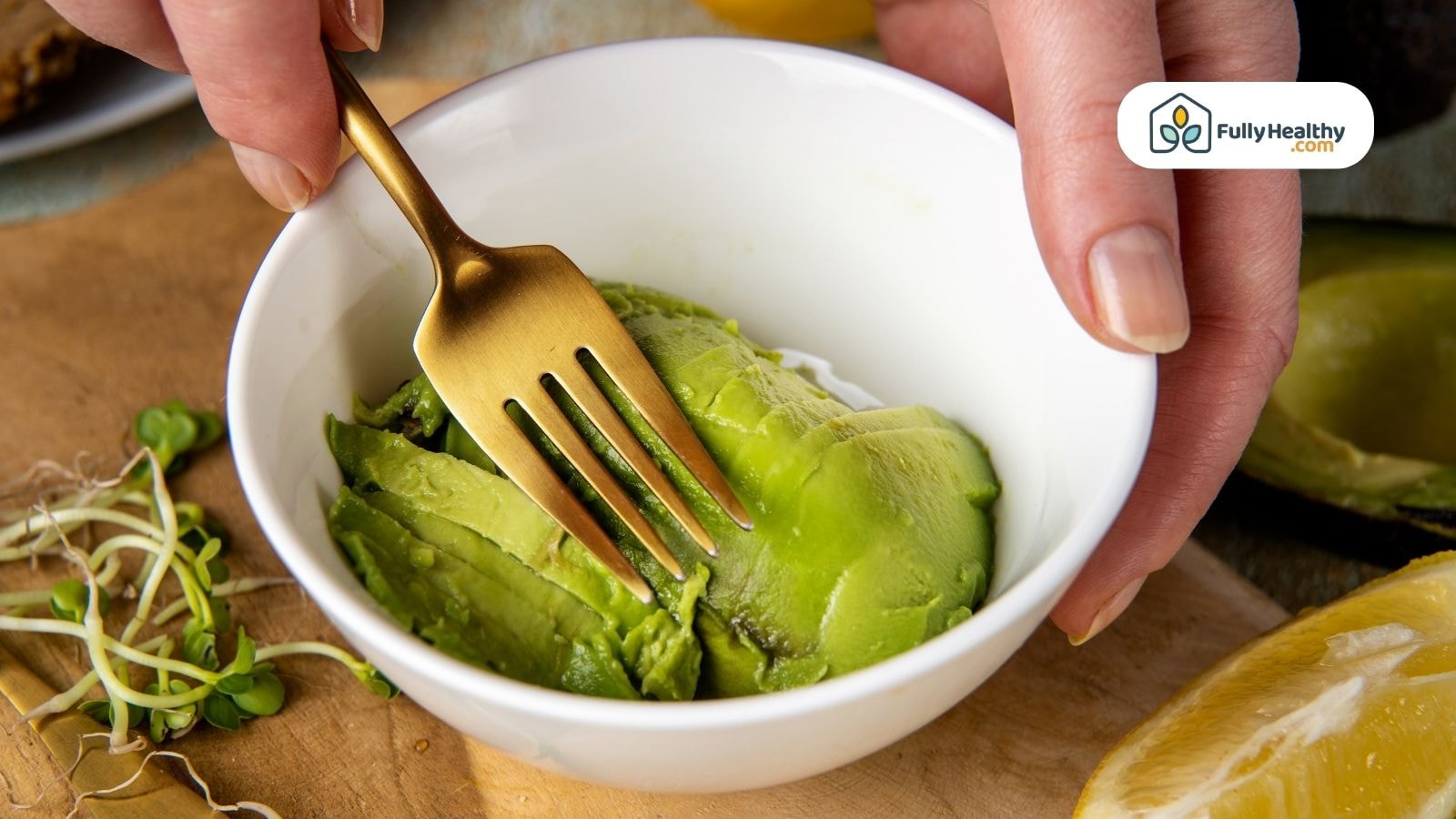 Person mashing fresh avocado slices in small white bow