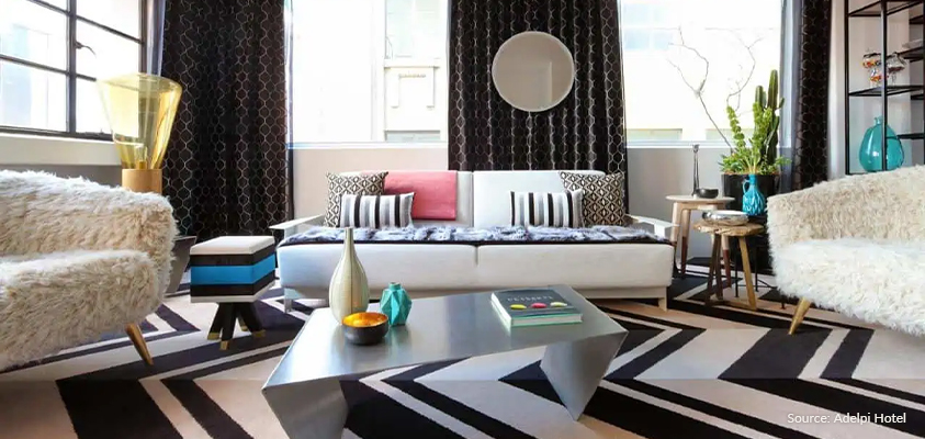 An Art Deco inspired living room in the Adelphi Hotel in Melbourne, Australia. Features black and white zigzag carpet, furry upholstery, chevron patterns, a silver coffee table and a white, black and blue licorice allsorts shaped ottoman.