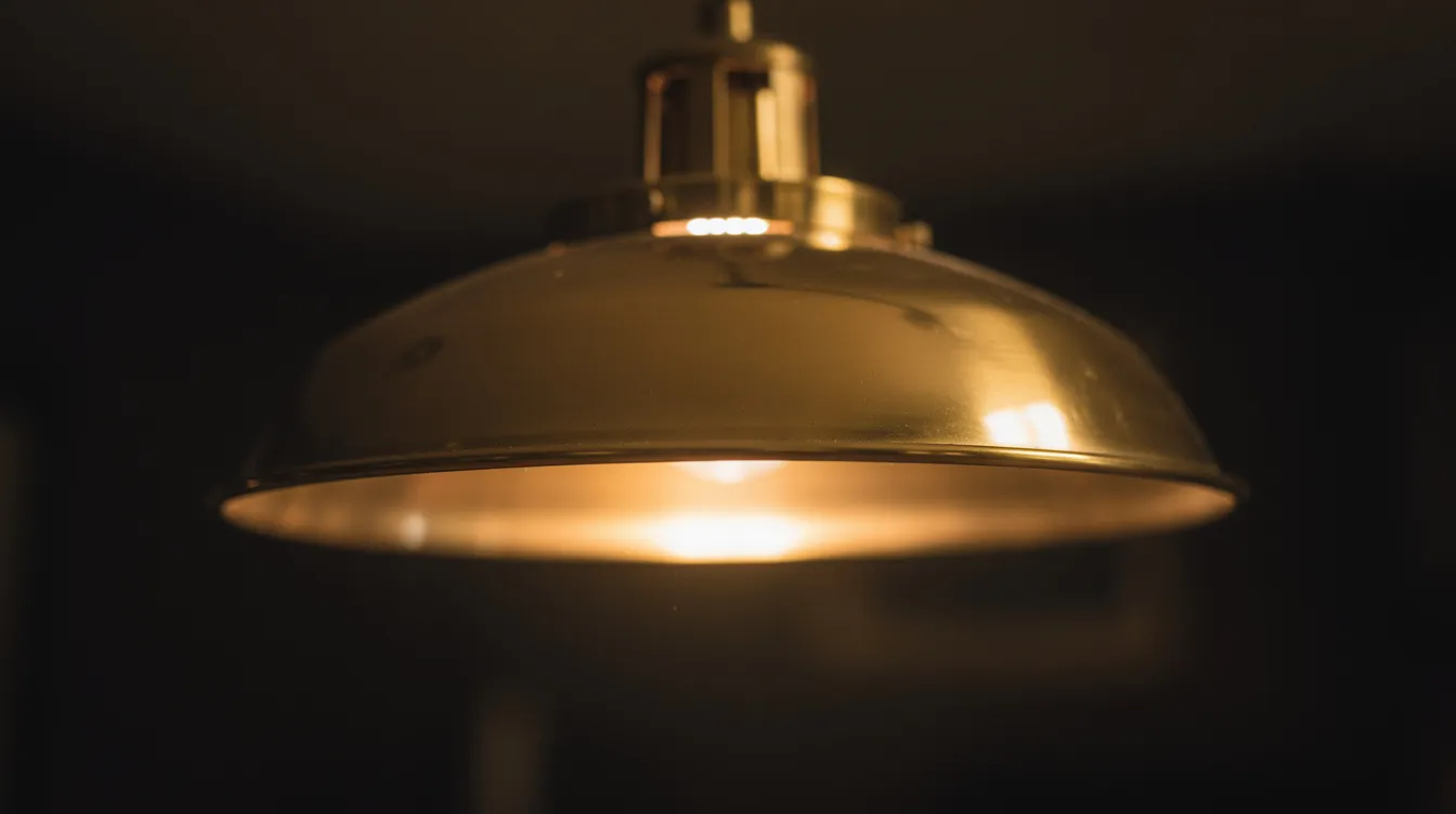 En närbild av en elegant pendellampa i mässing som avger ett varmt ljus mot en mörk bakgrund, vilket skapar en mysig atmosfär i rummet. Lampan är perfekt för att hänga över matbordet eller i vardagsrummet och bidrar till en stilren belysning.