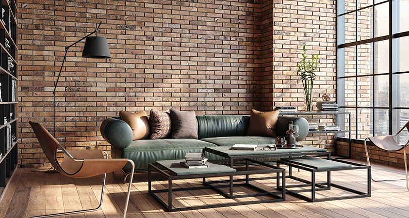 The exposed brick wall of this living room matches perfectly with the brown leather chairs and throw pillows, and highlights the green leather couch.