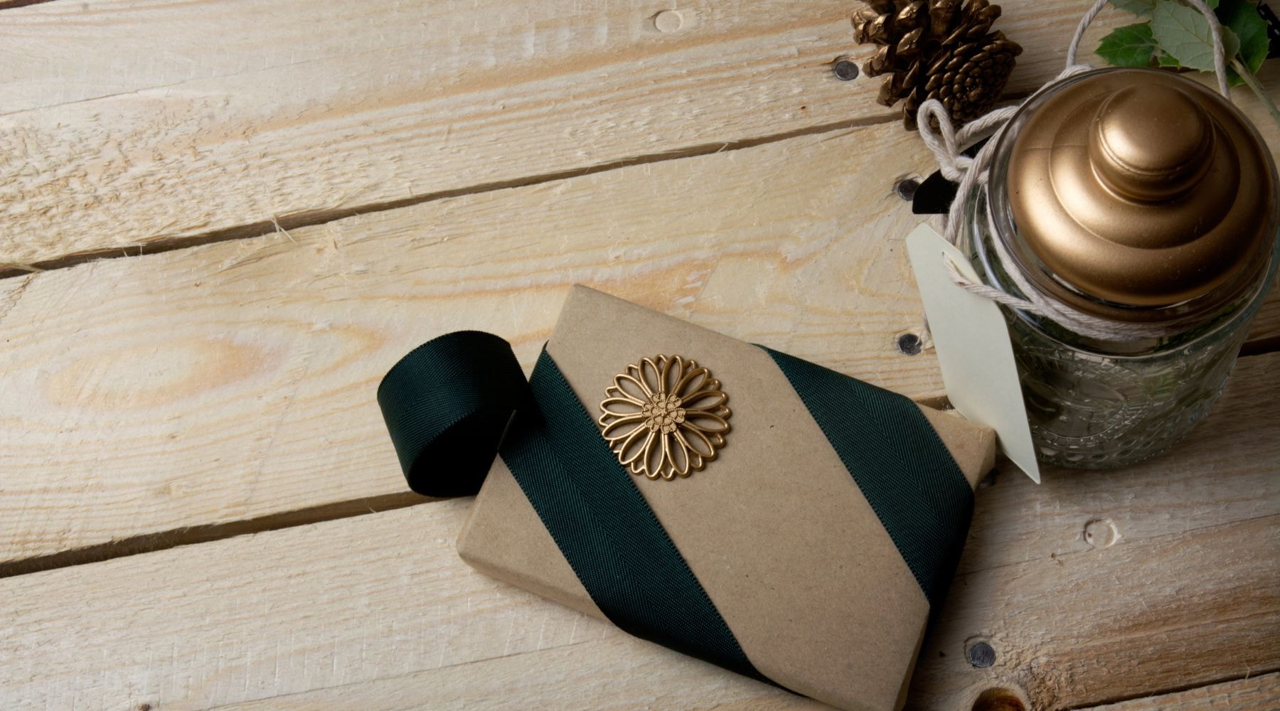 Kraft paper wrapped gift tied with a dark green ribbon and a decorative gold flower on a rustic wood background.