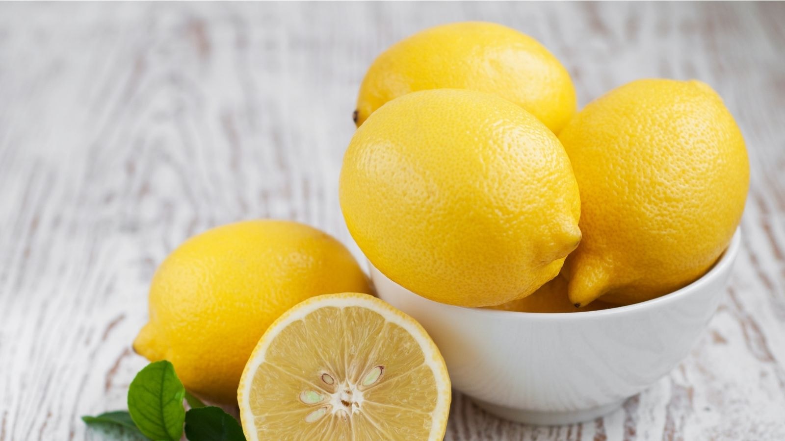 Ripe lemons in a white bowl with a sliced lemon