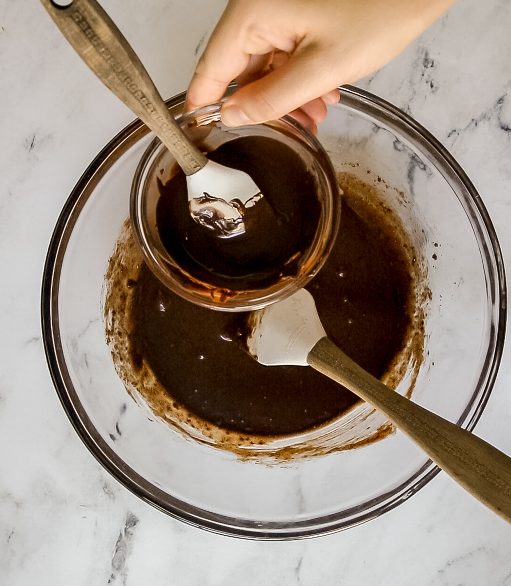 melted chocolate chips in small bowl being added to mixing bowl of double chocolate crinkle cookie batter