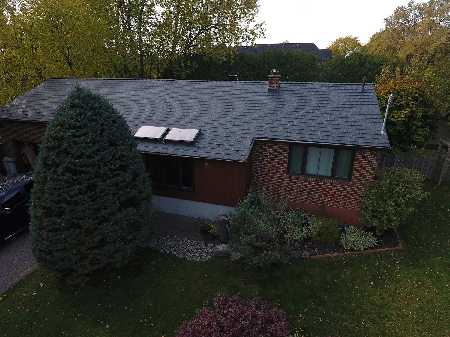 A residential home with a dark metal roof installation, surrounded by lush greenery and shrubs.