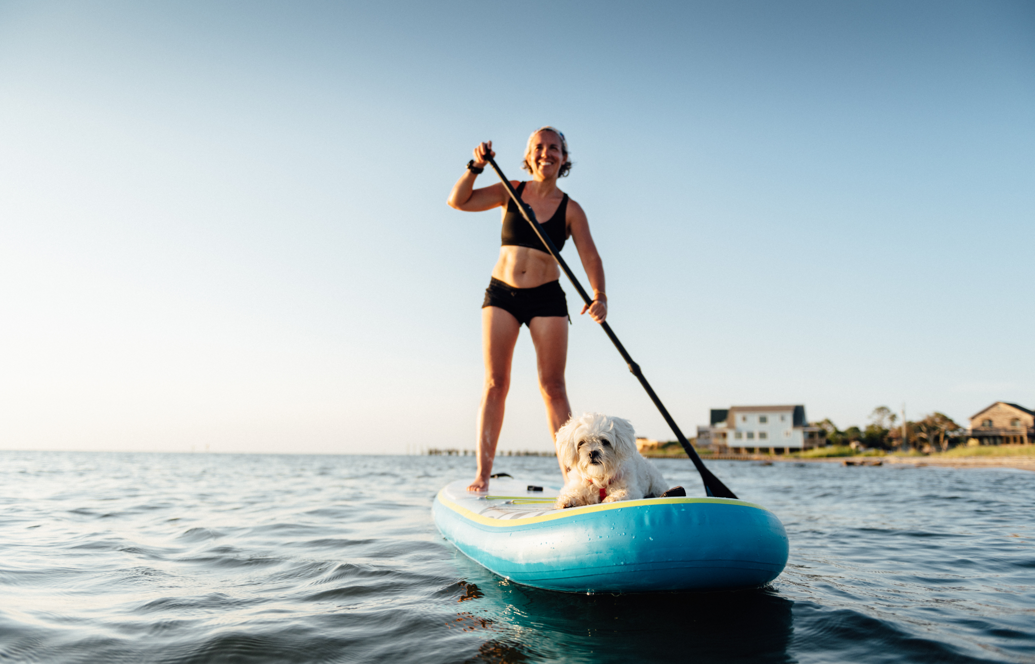 Woman on paddle board with small white dog - Adventure Wise Travel Gear