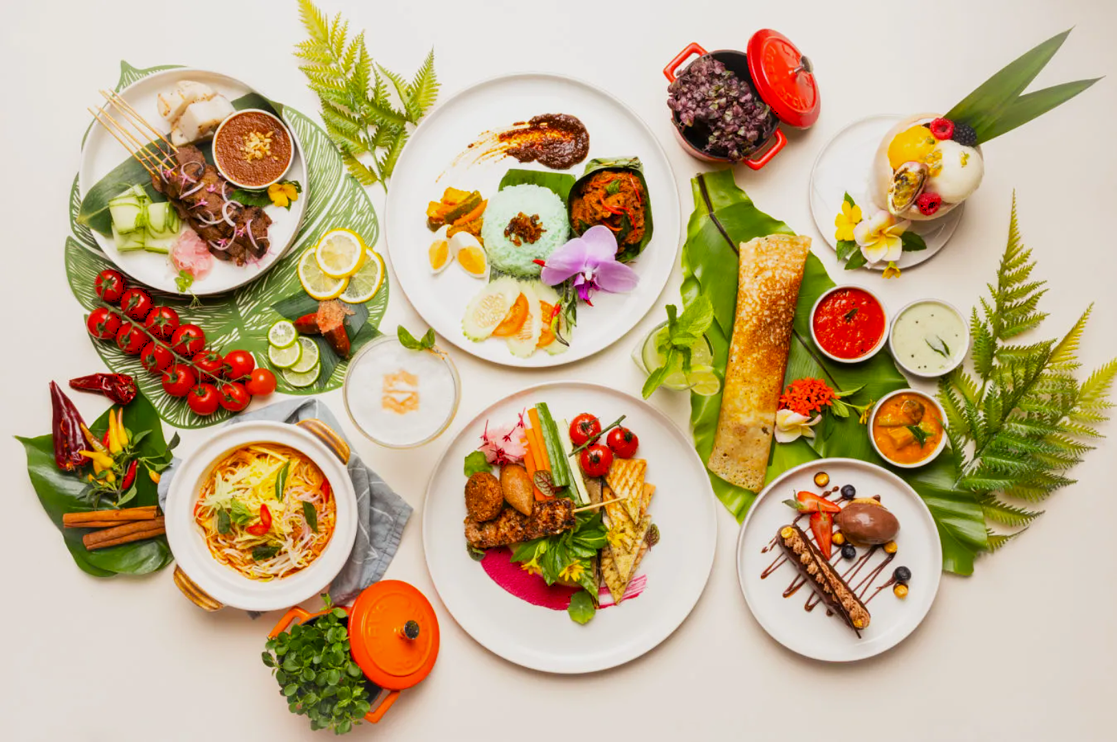 A vibrant flat lay of diverse gourmet dishes on white plates, surrounded by fresh greenery. Includes colorful salads, skewers, soups, desserts, and sauces.