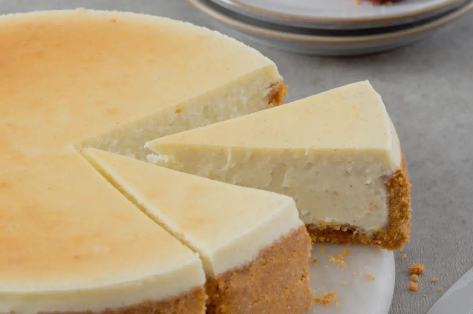 A slice of cheesecake is cut from a round cheesecake on a white plate.