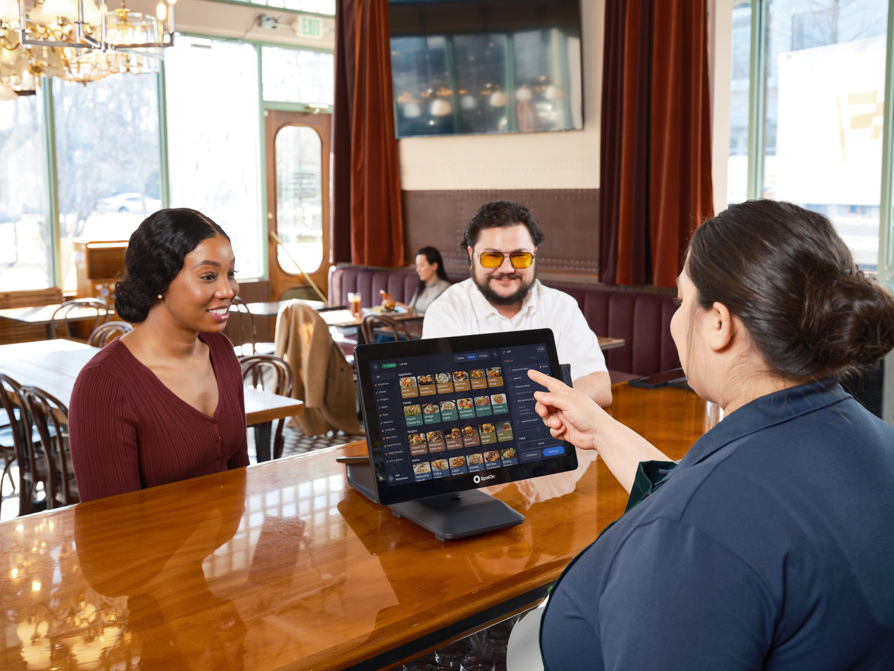 In a bustling restaurant setting, a restaurant owner is intently looking at a tablet, likely analyzing sales data or customer preferences, while staff members serve guests in the background, enhancing the overall dining experience. This scene highlights the integration of AI tools in the restaurant industry, showcasing how technology can improve operational efficiency and customer satisfaction.