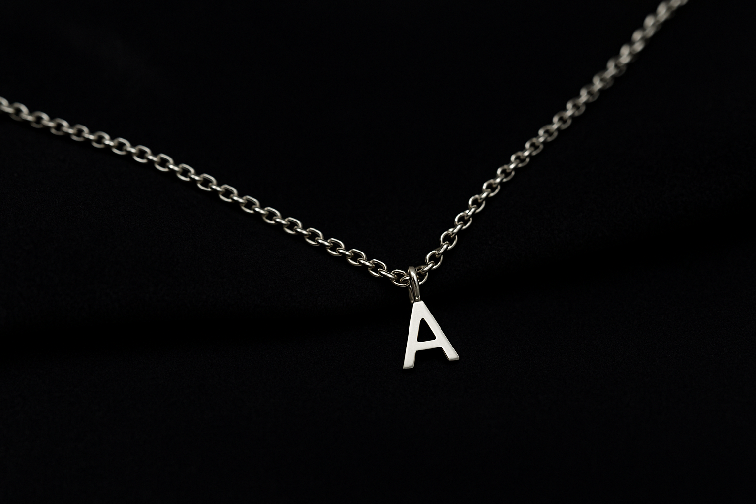 Vyriška auksinė grandinėlė su raidelės pakabuku ant tamsaus fono