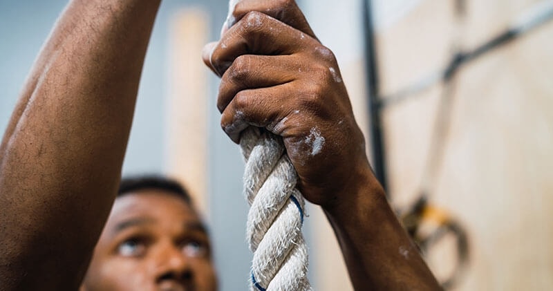 A man climbing a rope during a strength workout at a local gym.