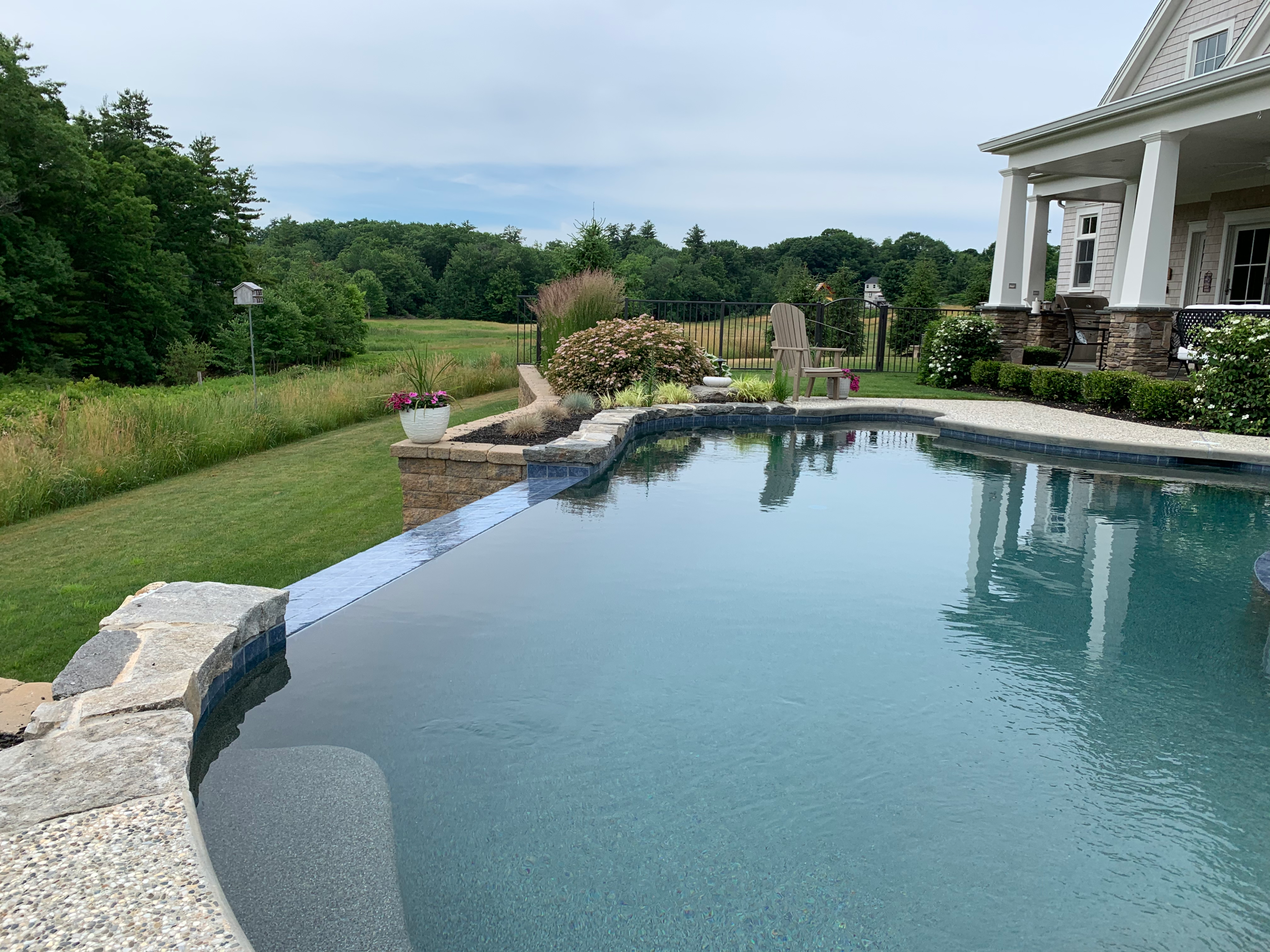 Sophisticated outdoor living space with a gunite pool as the centerpiece, surrounded by comfortable seating and lush landscaping, showcasing the transformative appeal of gunite pools in enhancing backyard luxury and livability.