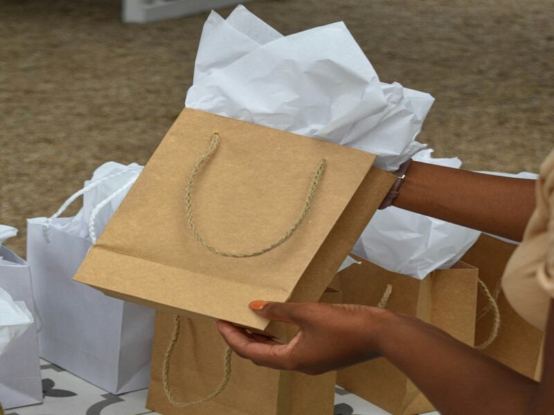 Small brown paper bags for gifting. They bags have rope handles and white tissue paper, perfect for parties, events, or retail packaging. These stylish bags are not only promote eco-friendliness but also depicts style. These are also reusable, making them ideal for presenting gifts or favors in a simple, elegant, and sustainable way.