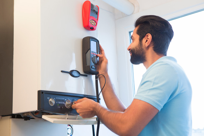 Techniker bedient Heizungssteuerung mit Messgerät an der Wand.