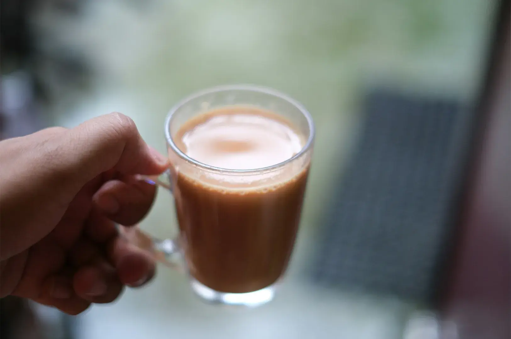 Hand holding a glass mug of milk tea.