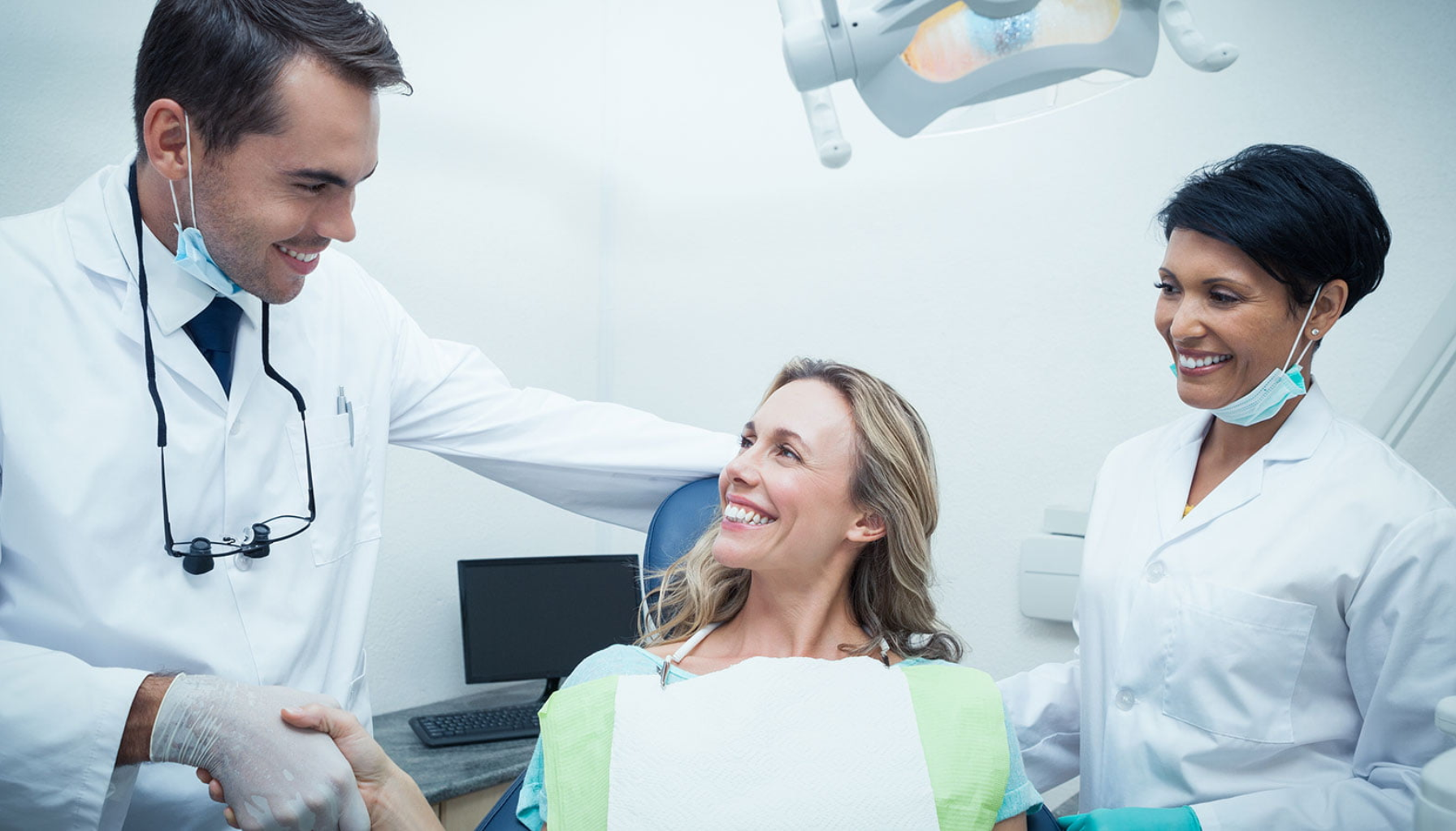 HELFO og Tannlegeskrekk: Du Har Rett På Hjelp – Både Psykisk og Økonomisk 7 Pasient smiler mens hun hilser på tannlege, med en tannpleier som står ved siden av i et lyst tannlegekontor.