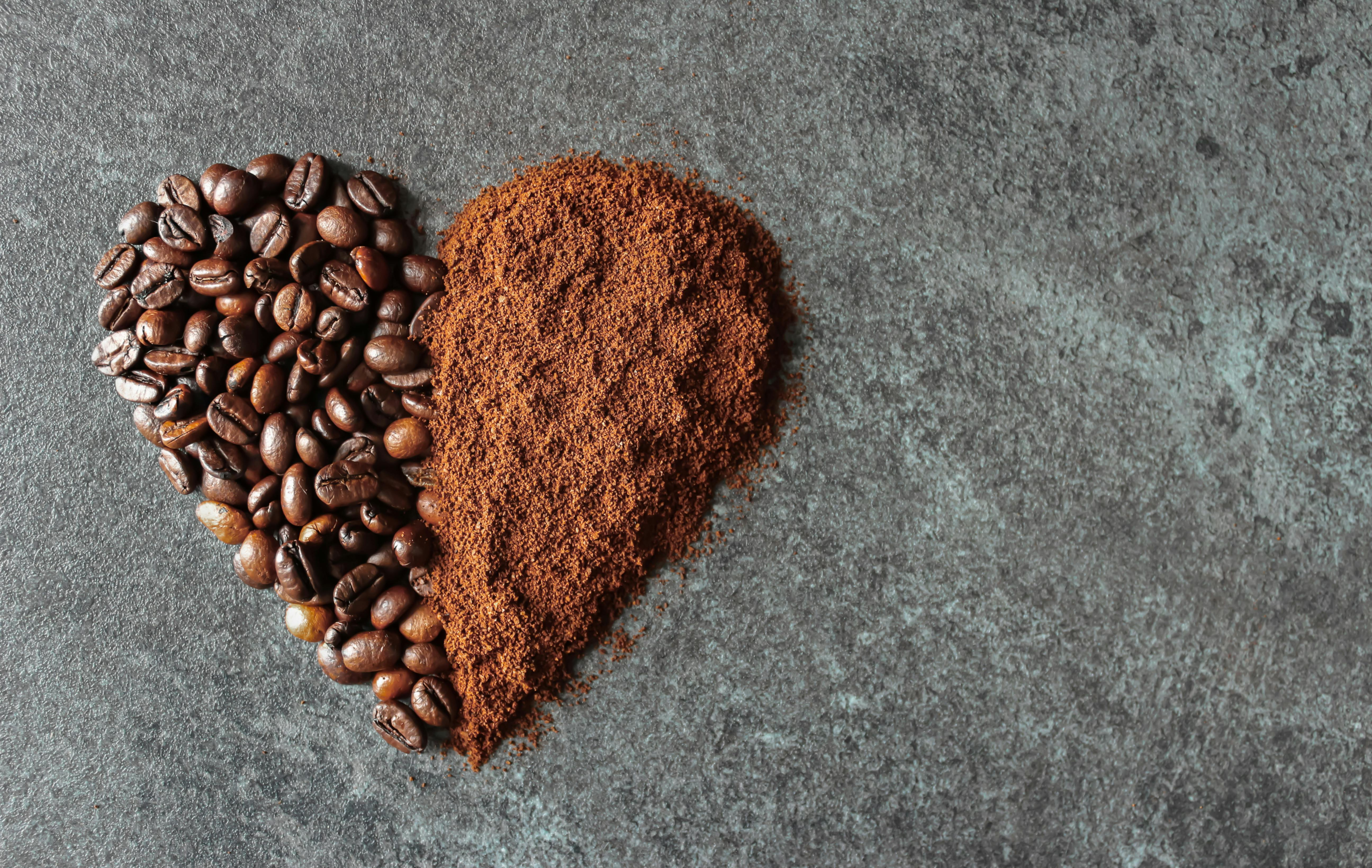 heart shape filled with brown coffee beans and fine coffee grounds on granite background