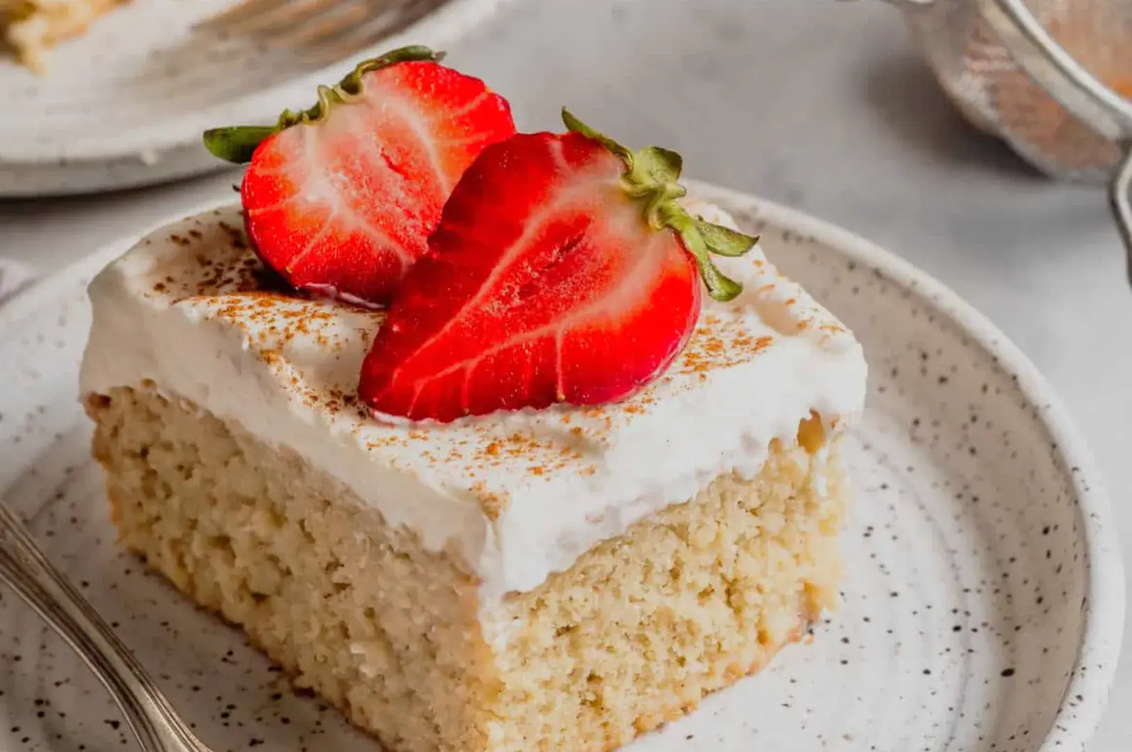 A slice of cake topped with whipped cream and fresh strawberries on a speckled plate.