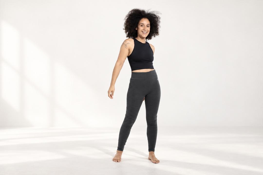 Frau in dunkelgrauen Orbasics-Leggings und schwarzem Oberteil in einem hellen Studio.