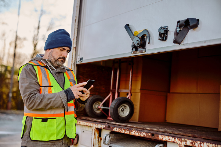 Man in a yellow and orange safety vest sending a text. 