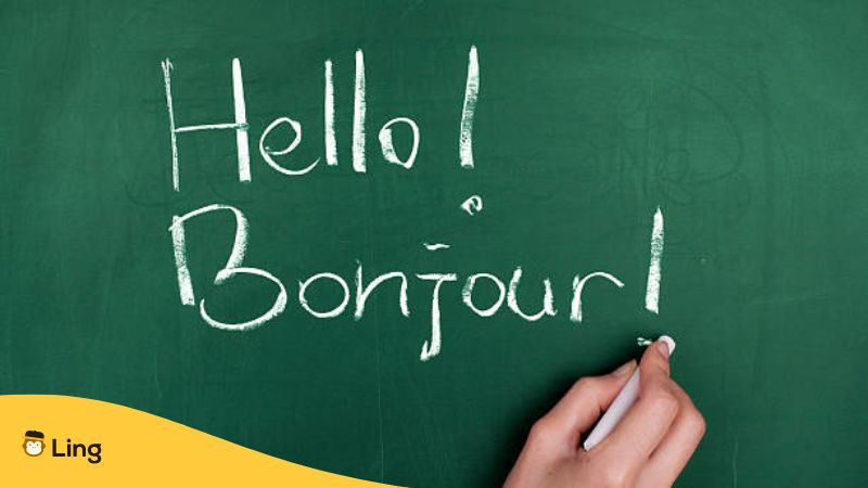 Woman hand writing ' Hello! Bonjour! ' on green blackboard