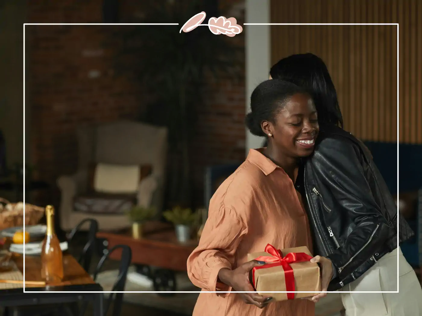 Two women embracing while one holds a gift wrapped in brown paper with a red ribbon. Fabulous Flowers and Gifts.