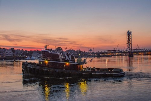 Tugboat steaming through dusk by downtown Portsmouth, New Hampshire