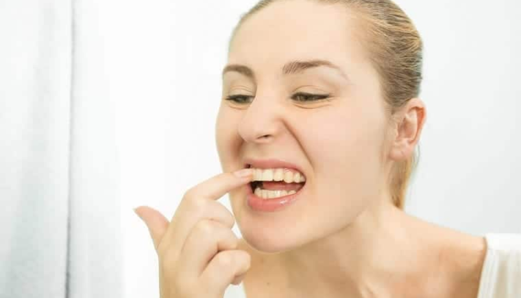 Pyrea: Den stille tannkjøttsykdommen som kan koste deg tennene 11 Kvinne ser i speilet og peker på irritert område ved tannkjøttet mens hun undersøker munnen nøye.
