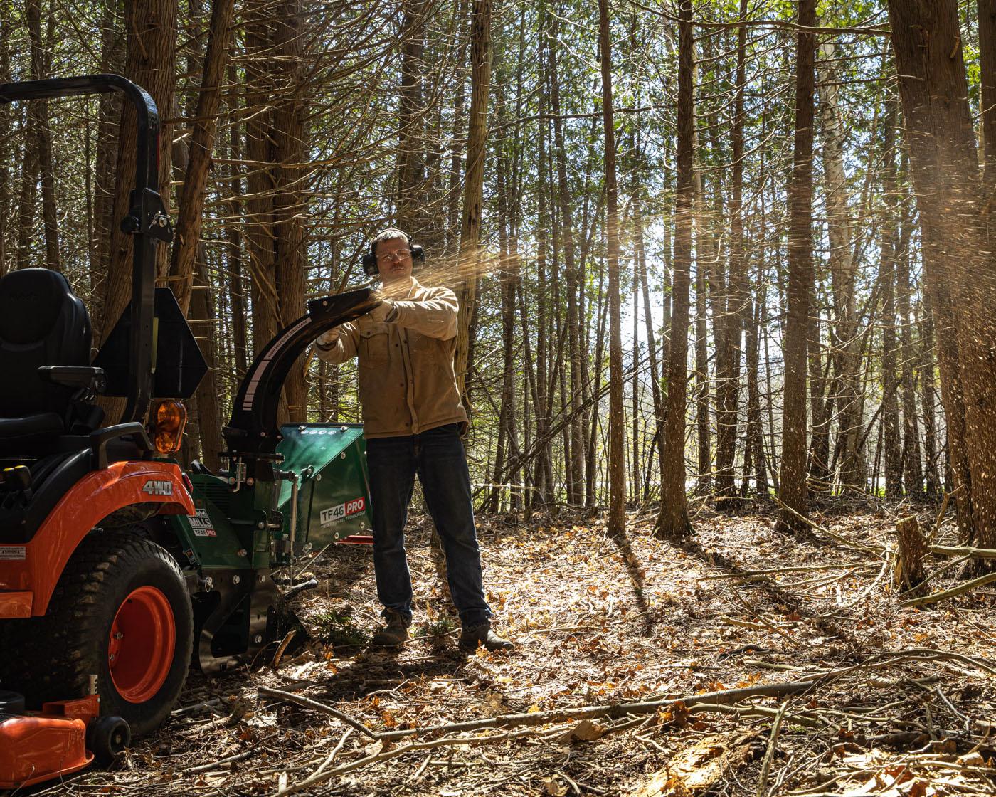 A Woodland Mills TF46 PRO Wood Chipper throwing wood chips on a wooded property.