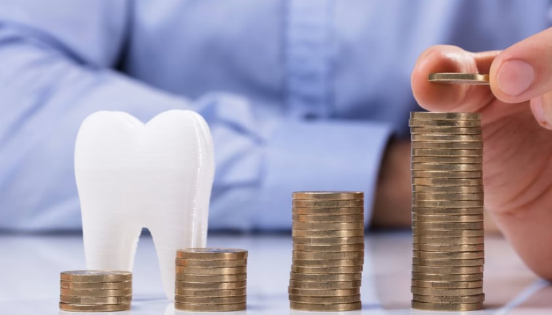 Stablede mynter i stigende høyde ved siden av en tannmodell illustrerer økende kostnader for tannbehandling. Hånd legger på en ekstra mynt.
