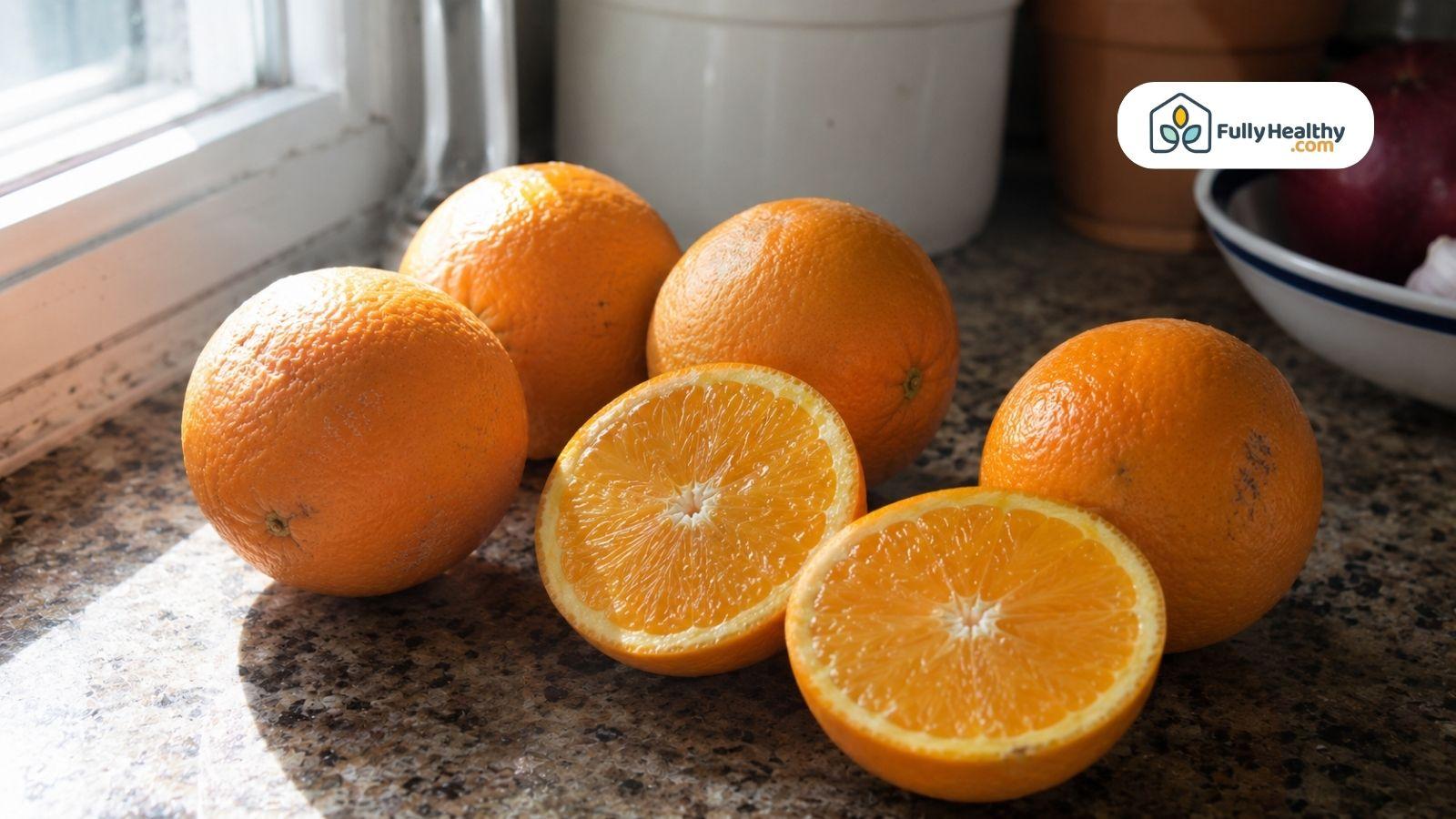 Fresh whole and sliced oranges displayed on a kitchen counter near a window.