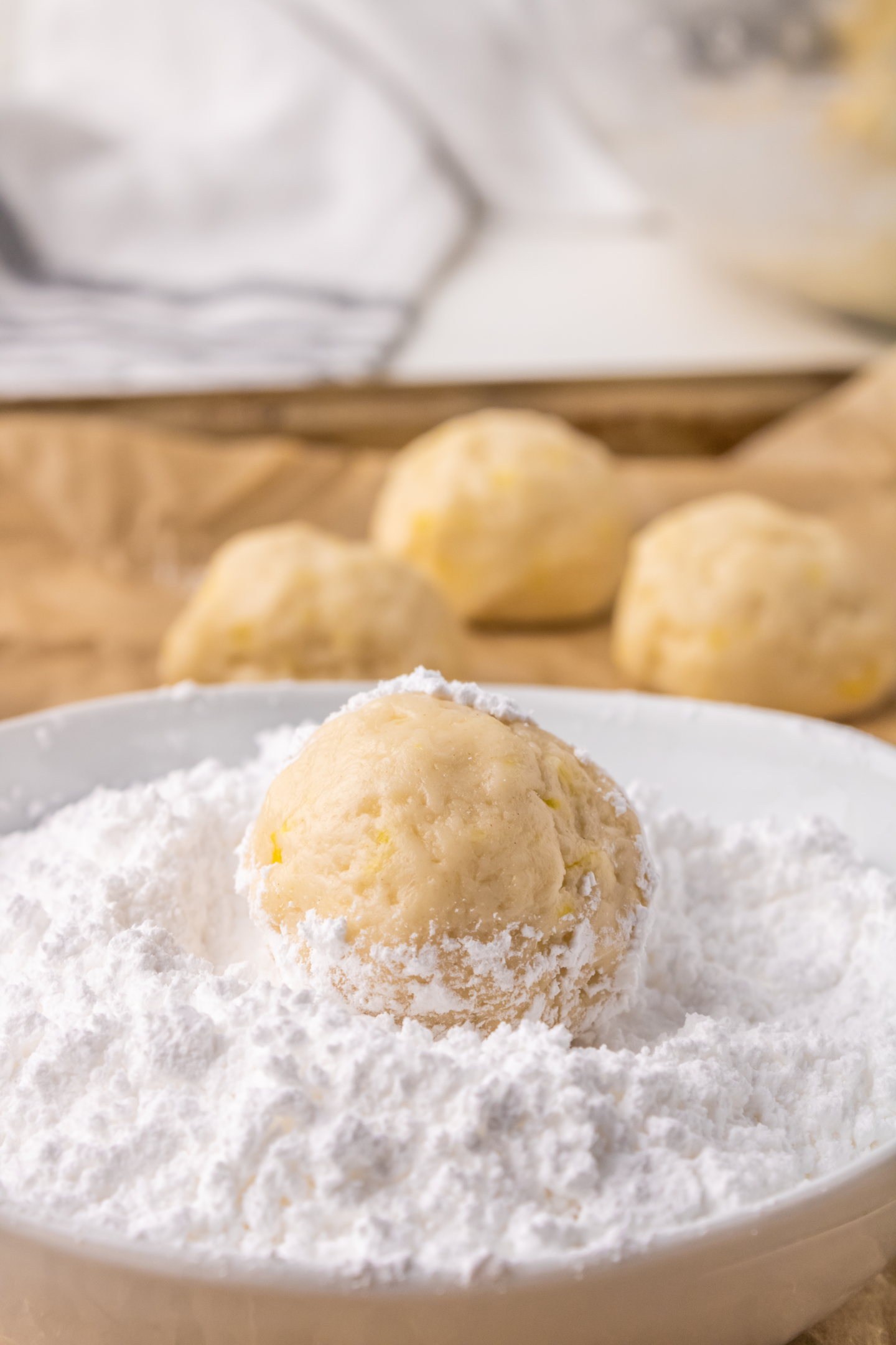lemon crinkle cookie dough ball in a medium bowl of powdered sugar