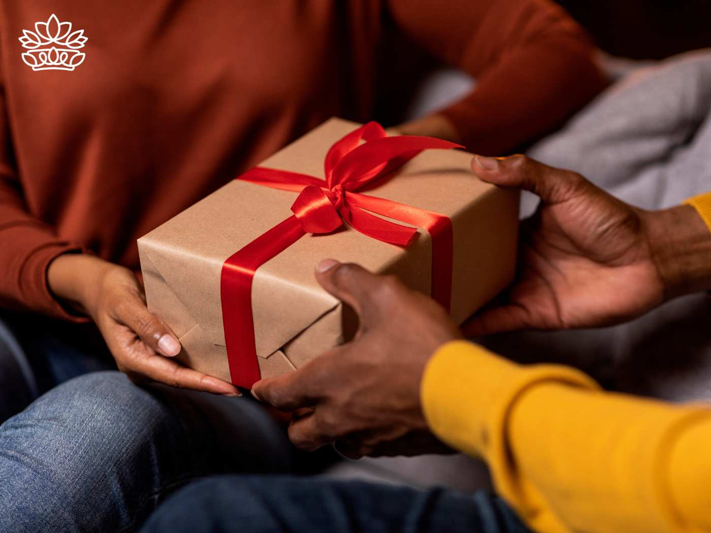 Close-up of hands exchanging a beautifully wrapped gift box with a red ribbon, symbolizing caring and sharing within the Gift Boxes by Recipient Collection from Fabulous Flowers and Gifts.