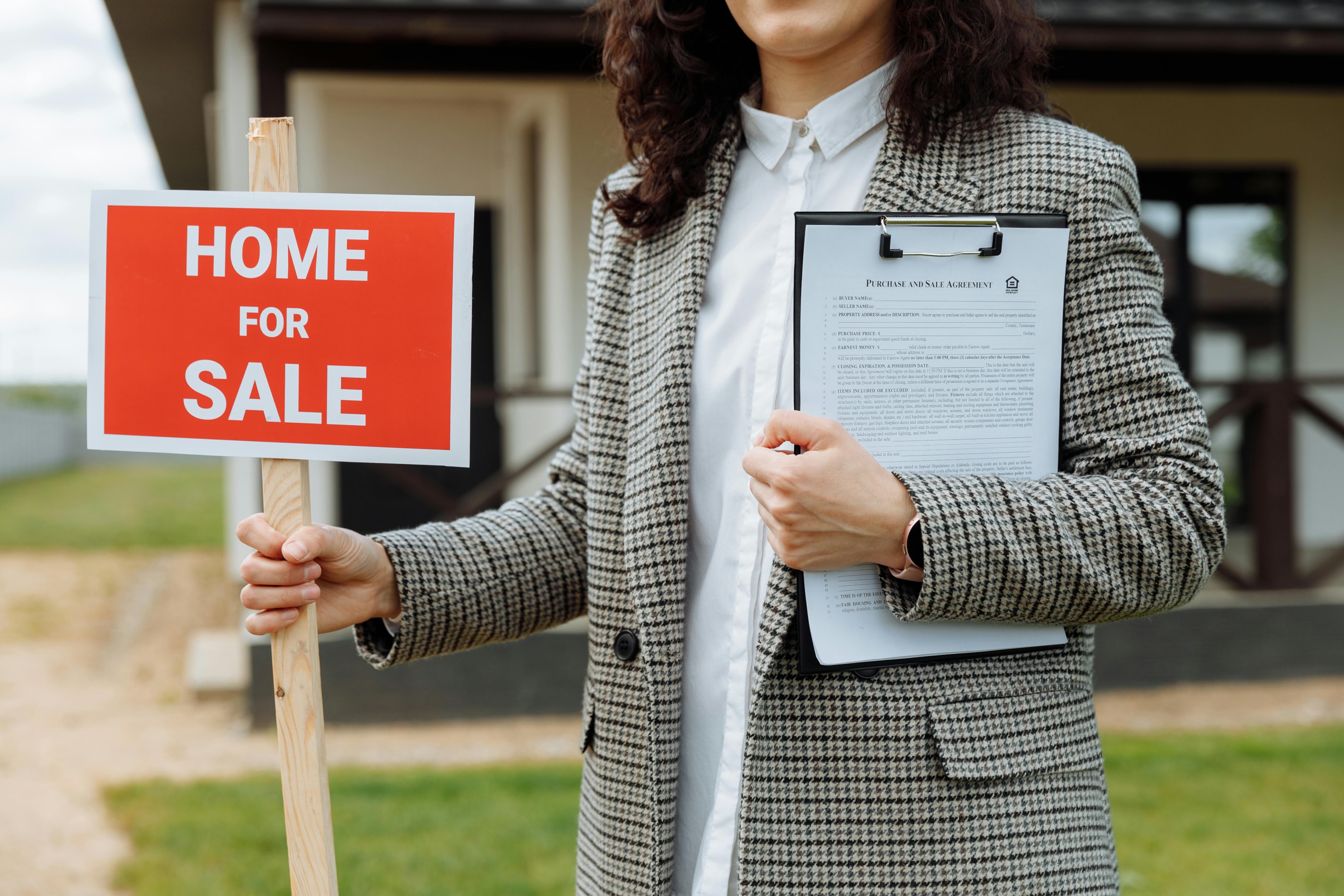 Real estate professional with 'Home for Sale' sign in front of renovated house. 