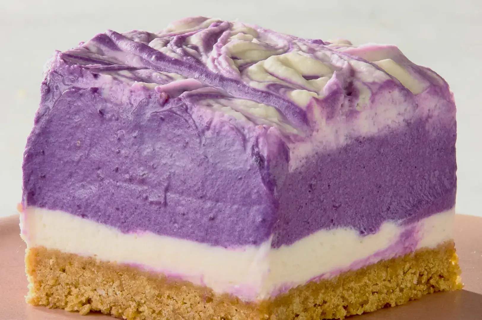 A slice of layered purple dessert with a crumbly base and swirls of creamy frosting on top.