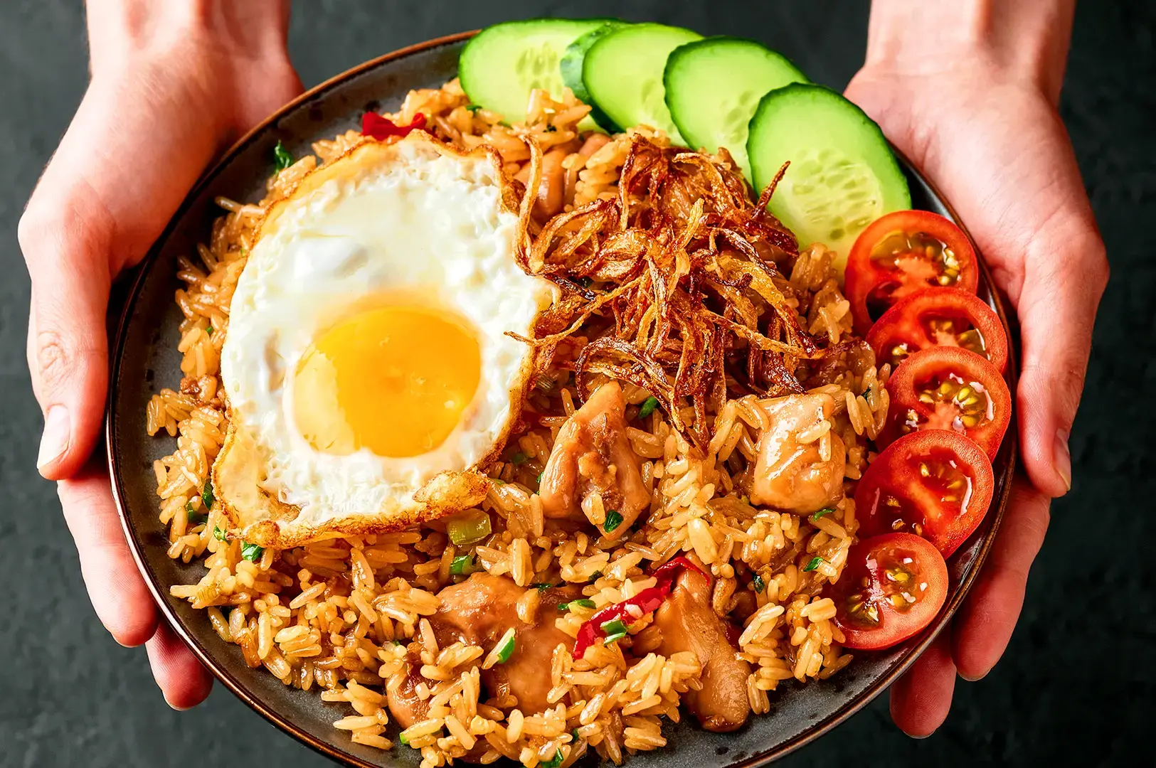 Indonesian nasi goreng with fried egg, crispy shallots, cucumber and tomato served on a plate