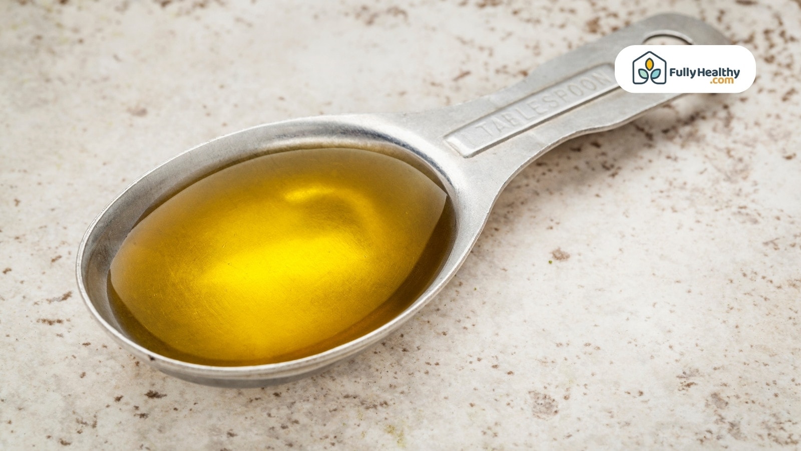 Tablespoon filled with olive oil on light stone surface