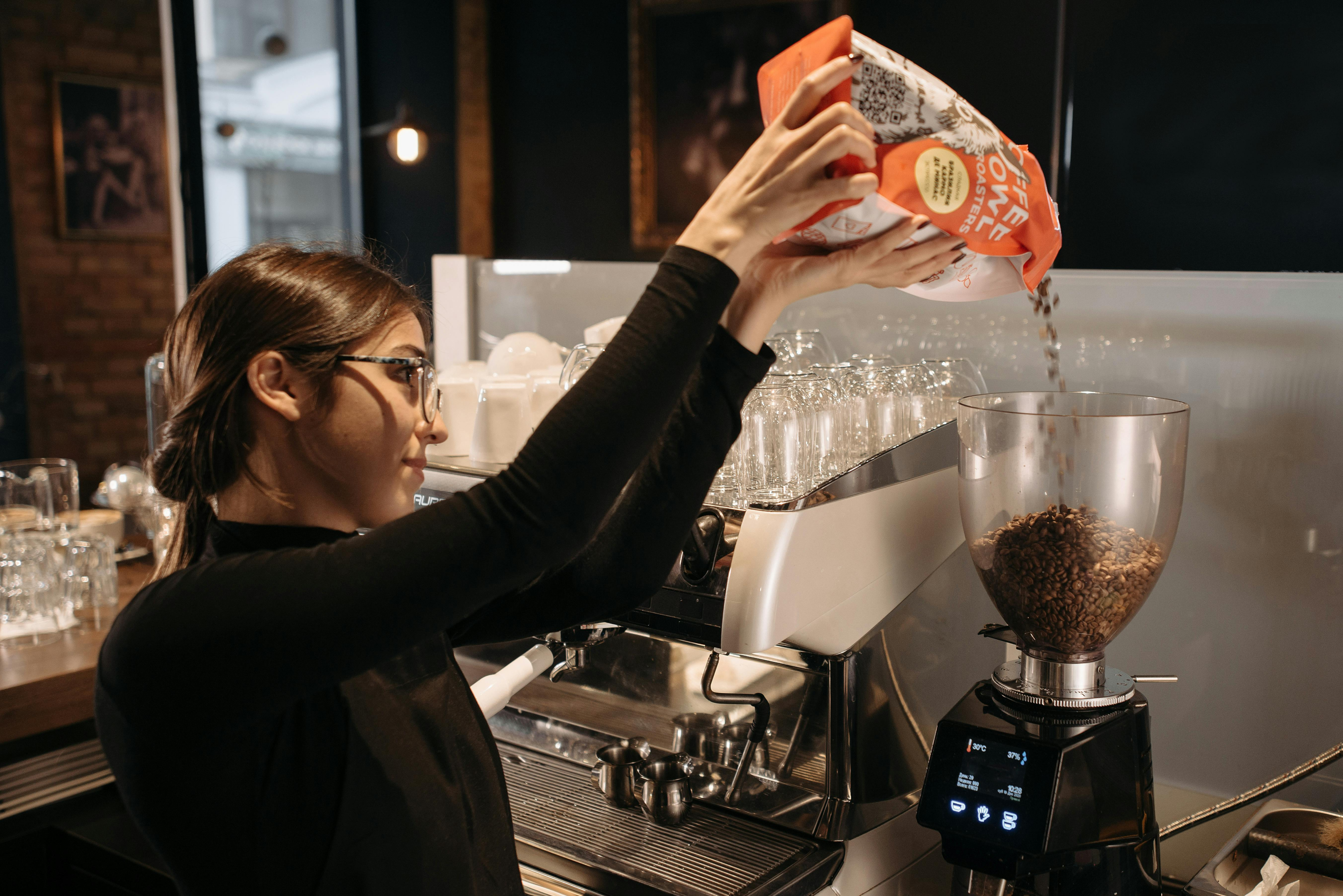 barista pouring coffee beans into the hopper of an electric coffee grinder