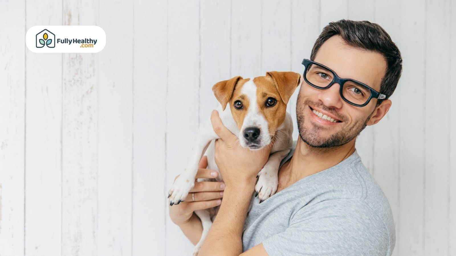 Man holding small dog smiling against white wooden background