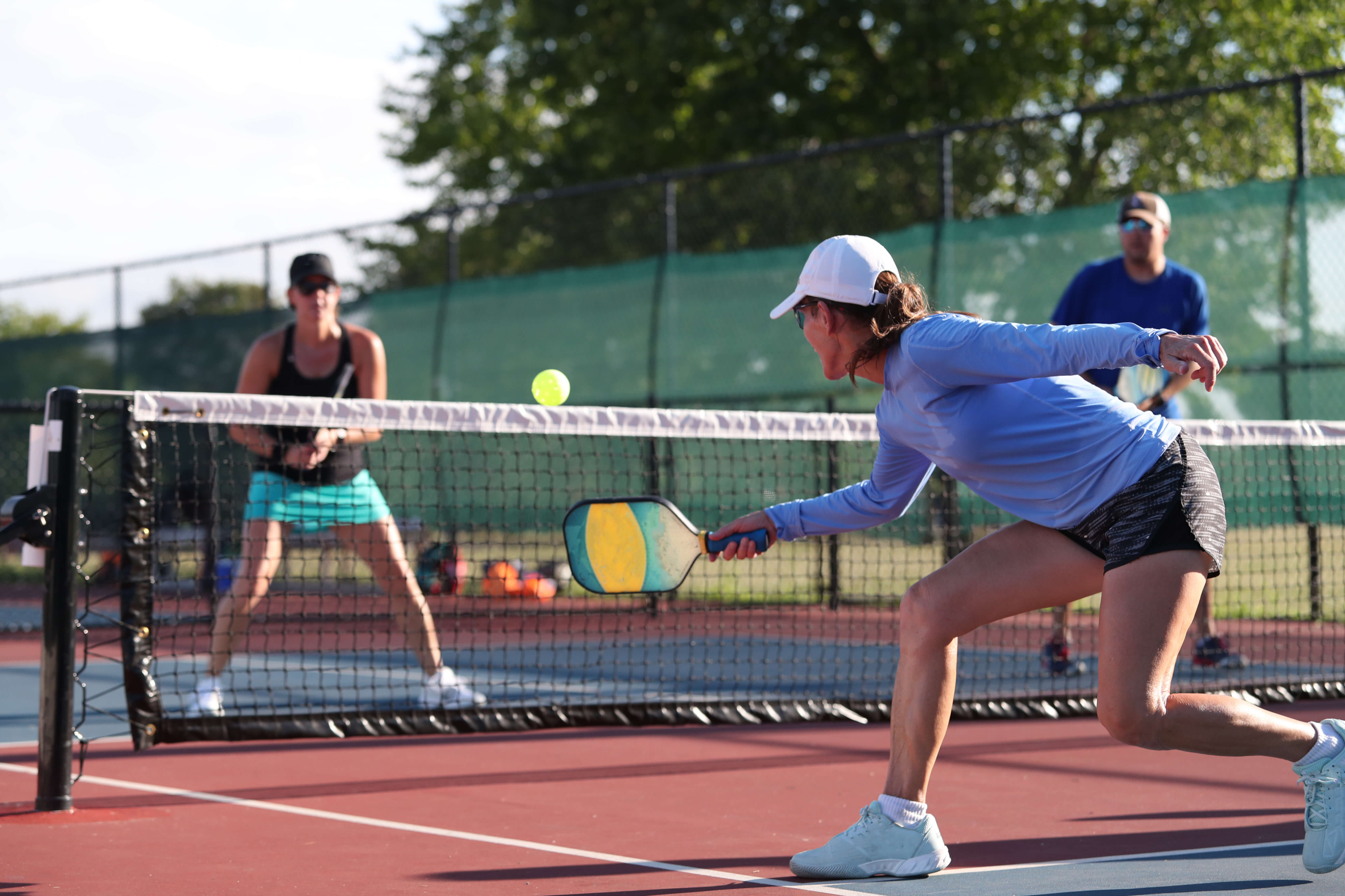 An enthusiastic woman preparing to strike a pickleball with her paddle during a game.