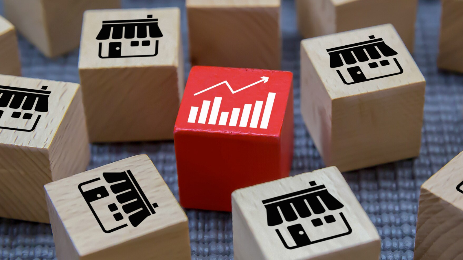 Set of wooden blocks with storefront icons surrounding a red cube featuring a growth chart illustrating how scalable cloud PBX solutions support rapid expansion for multi-location businesses.