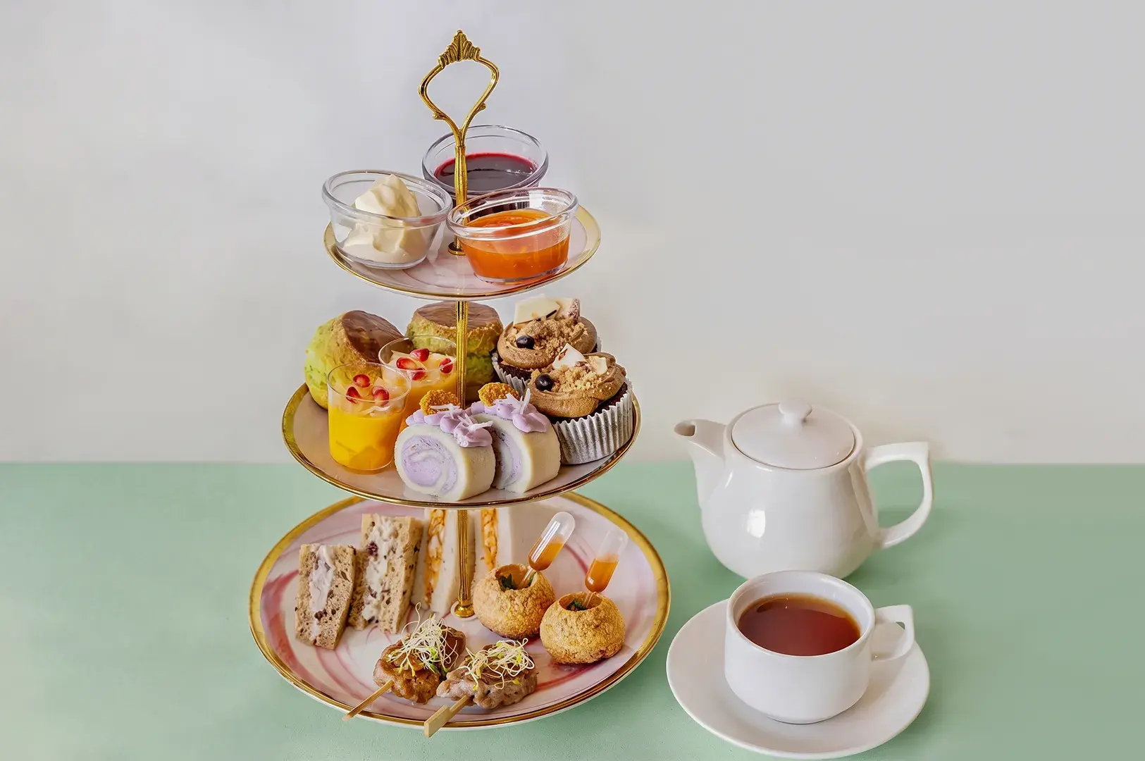 Three-tiered afternoon tea stand with sweet and savory bites, served with a white teapot and teacup.