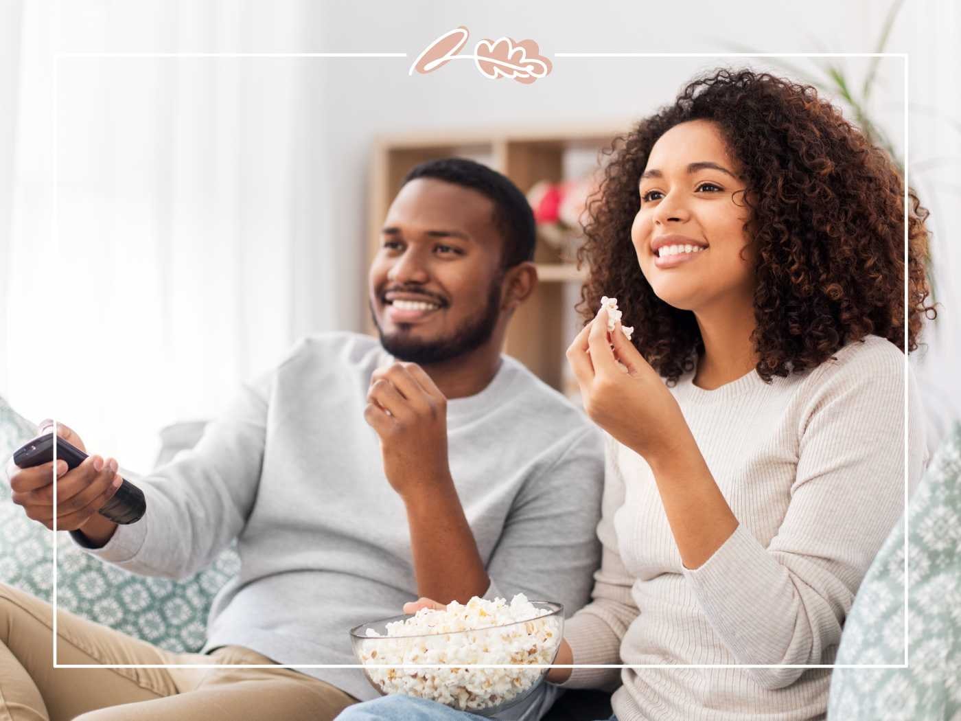 A smiling couple enjoying a cosy movie night at home, sharing a bowl of popcorn - Fabulous Flowers and Gifts.