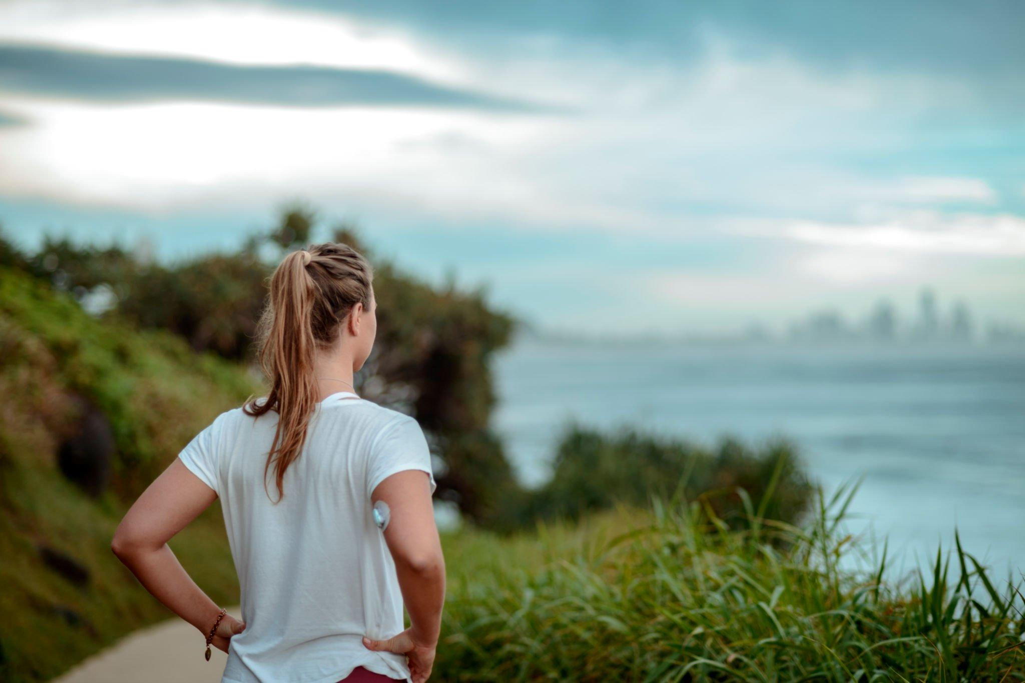 A person wearing a CGM device on their arm while gazing into the distance