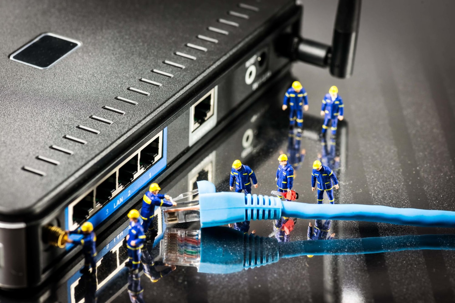 A creative concept showing tiny figurines in construction uniforms interacting with a network cable and router. The image represents call routing, cloud-based telecom, and managed telecom services.