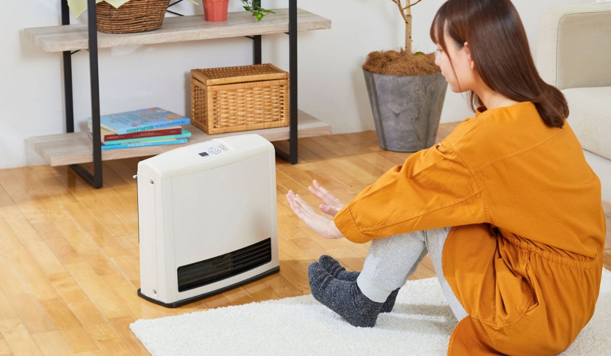 Figure in living room warming themselves in front of a convector heater