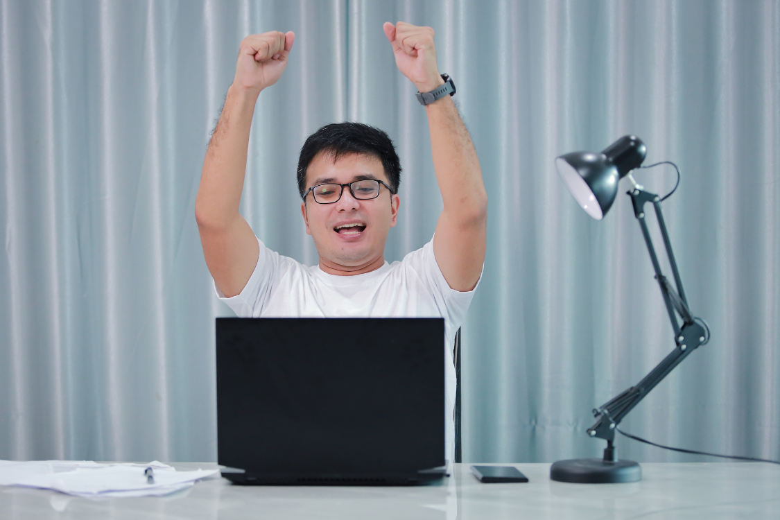 A joyful Filipino remote worker raising hands after a successful moment