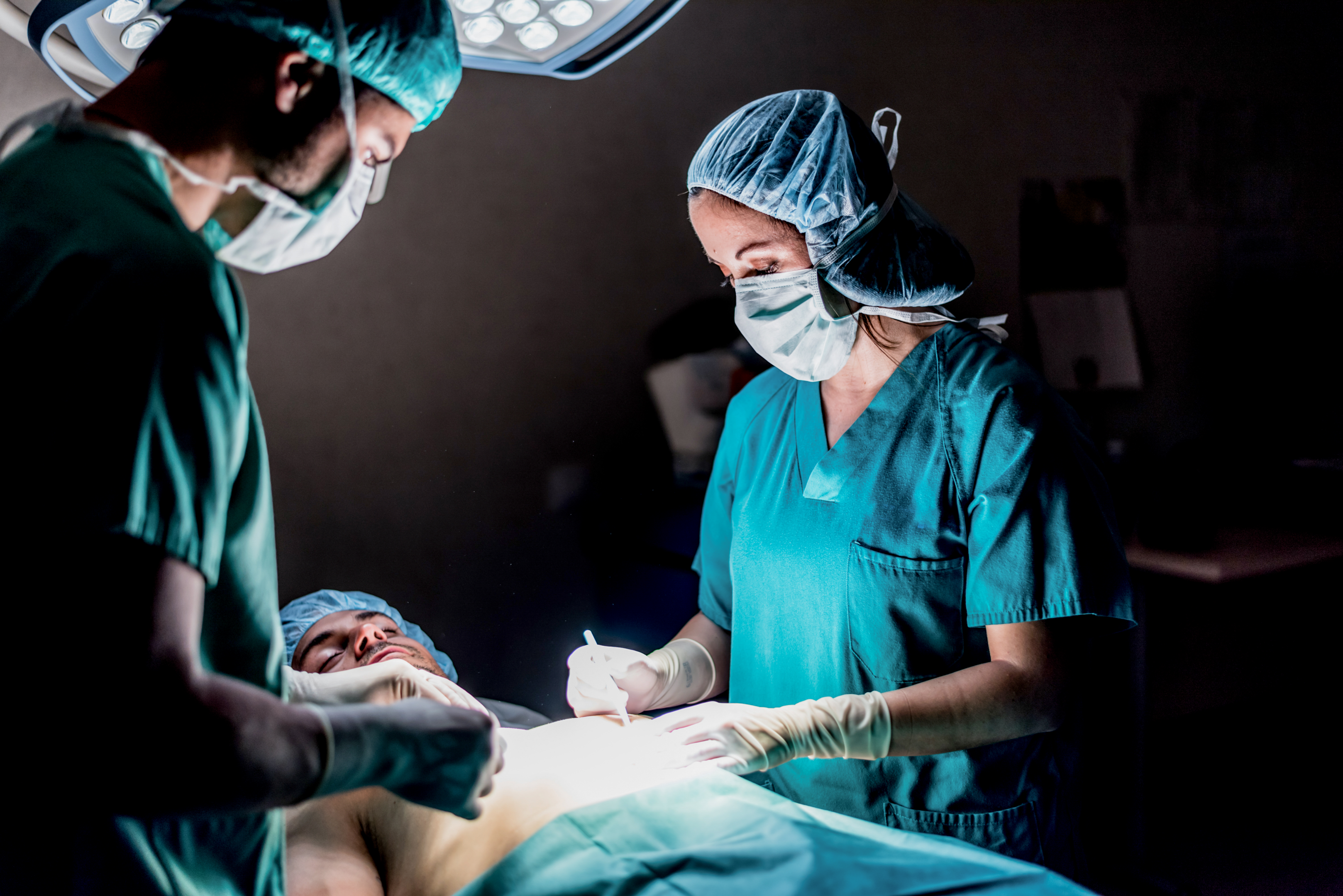 Two doctors in teal scrubs in the Operating Room standing over a sedated patient who is about to be in surgery.